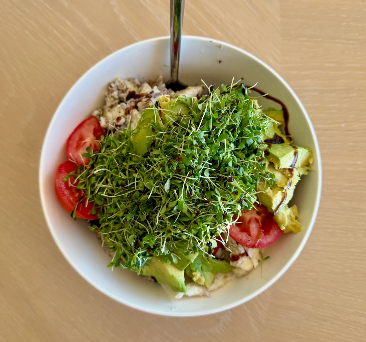 A white bowl with avocado, tomatoes, and a generous topping of fresh microgreens