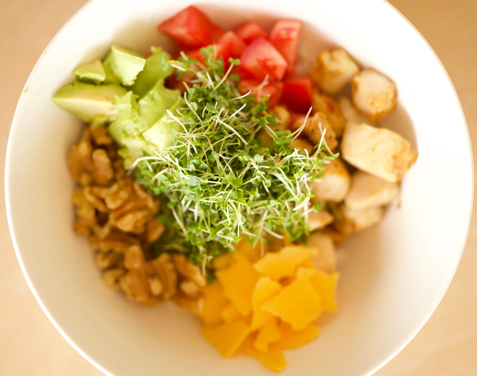 A bowl topped with microgreens, avocado, tomatoes, and yellow peppers
